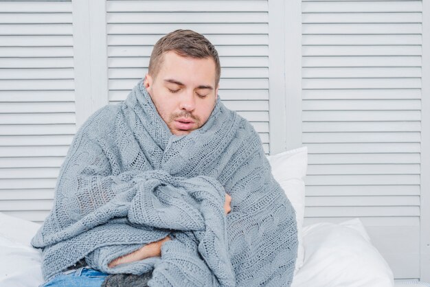 Young man wrapped in a warm scarf shivering from the cold