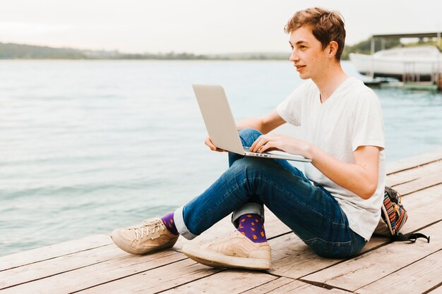 Young man writing on the laptop by the lake