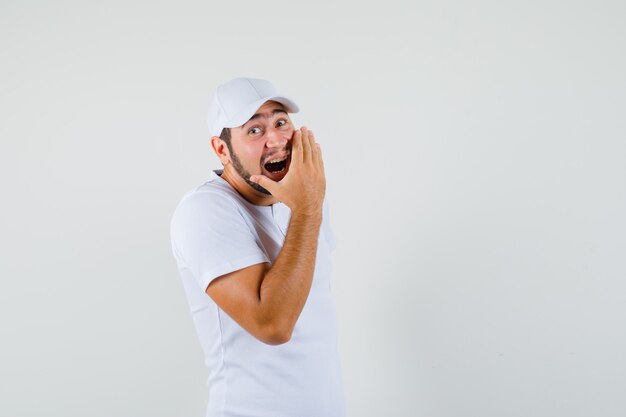 Young man yawning on his mouth with hand in white t-shirt and looking tired