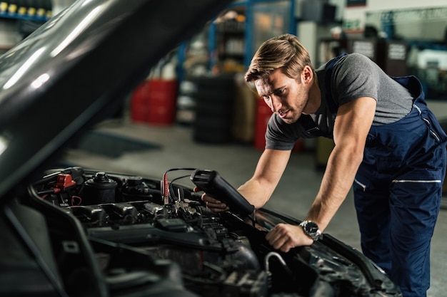 Young mechanic with diagnostic tool analyzing car engine problem in auto repair shop