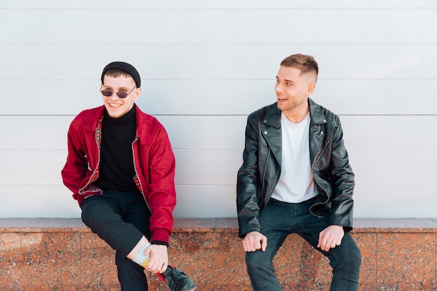 Free Photo young men sitting on parapet and smiling 