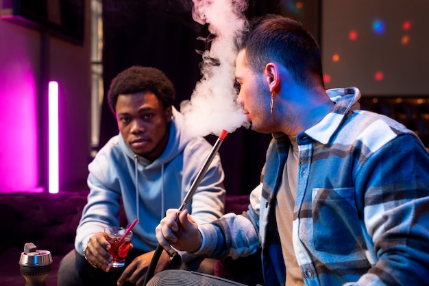 Free Photo young men vaping from a hookah indoors