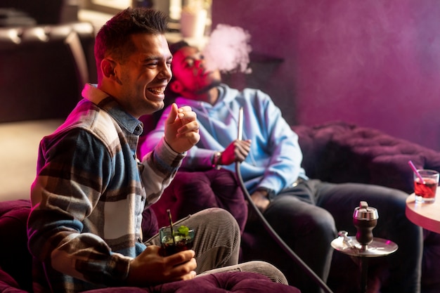 Young men vaping from a hookah indoors