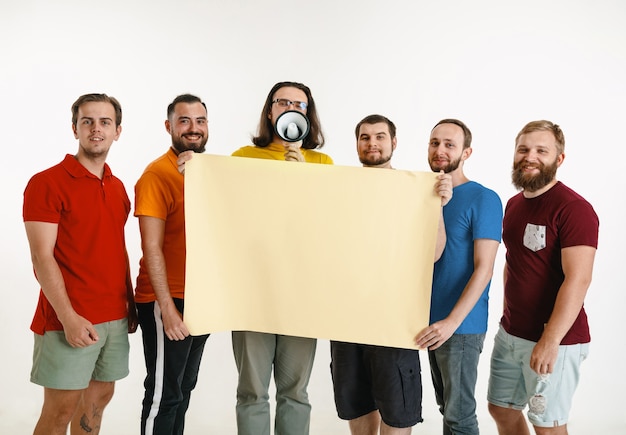 Young men weared in LGBT flag colors isolated on white wall. Caucasian male models in shirts of red, orange, yellow, green, blue and purple. LGBT pride, human rights, choice concept. Copyspace.