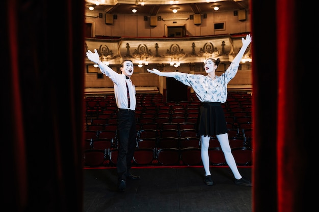 Free photo young mime couple standing on stage raising their arms