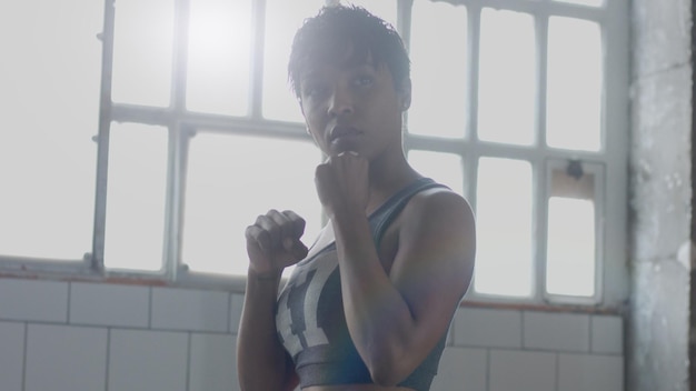 Free Photo young mixed race african american woman makes a boxing workout in sunny loft contour light looking throught the camera