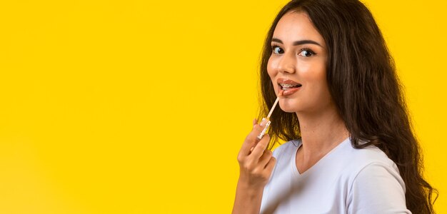 Young model applying lip gloss and smiling