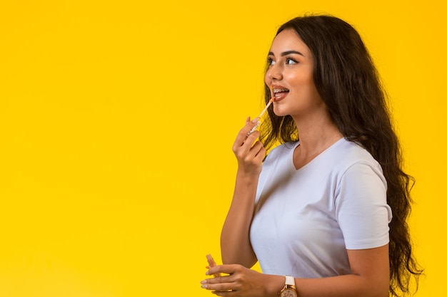 Young model applying lip gloss and smiling. 