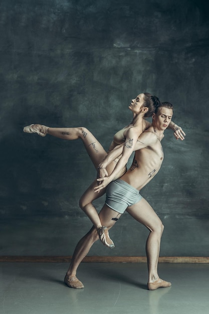 Free photo the young modern ballet dancers with tatoos on bodys posing on gray studio background