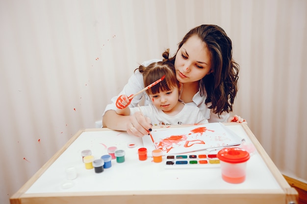 Free photo a young mother, along with her little daughter paints on paper