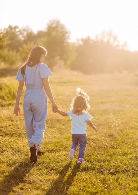 Young mother and daughter, hugging and playing in a golden field of sunshine