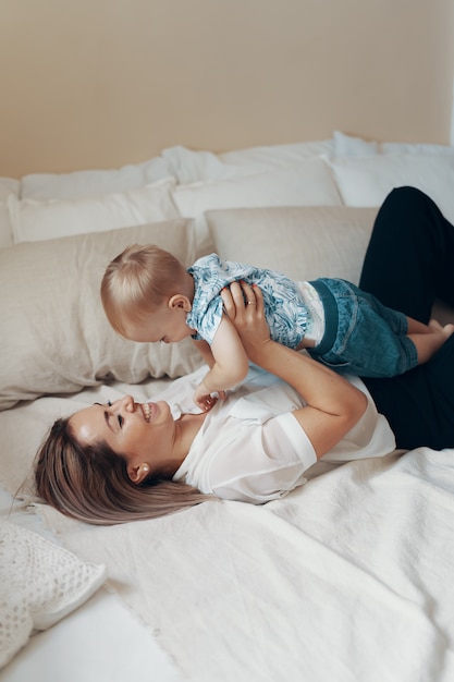 Young mother having fun laughing playing funny active games with cute child son in bedroom