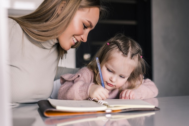 Young mother helping daughter with her homework at the table in the dining room