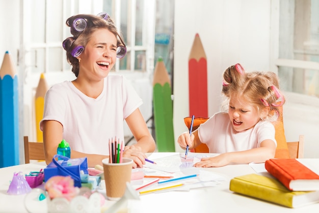 The young mother and her little daughter drawing with pencils at home