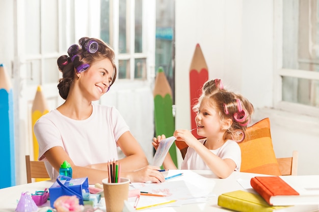 The young mother and her little daughter drawing with pencils at home