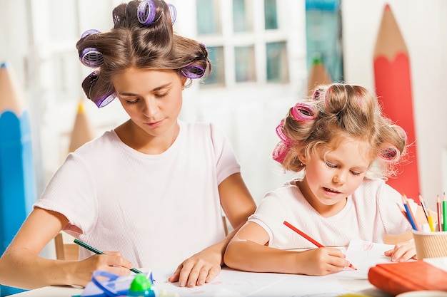 Free photo the young mother and her little daughter drawing with pencils at home