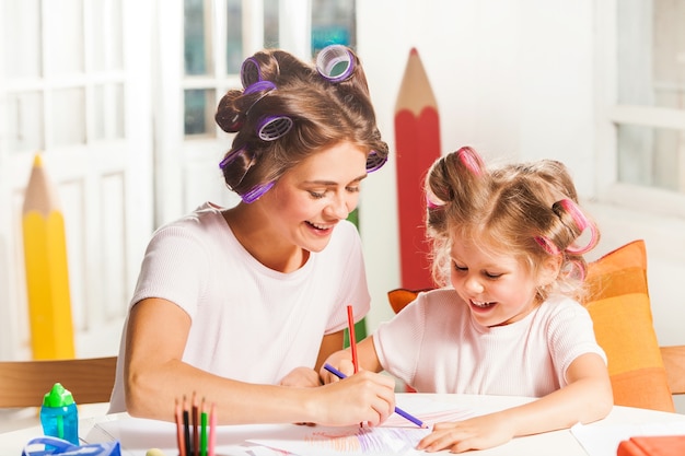 The young mother and her little daughter drawing with pencils at home