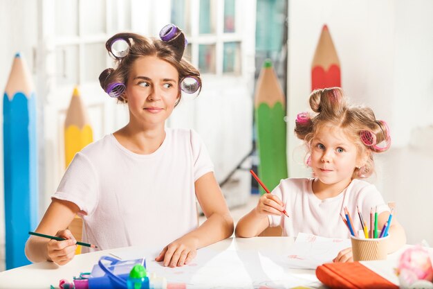 The young mother and her little daughter drawing with pencils at home