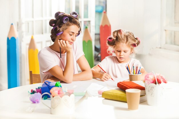 young mother and her little daughter drawing with pencils at home