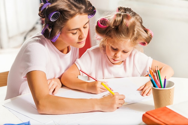 Free photo the young mother and her little daughter drawing with pencils at home