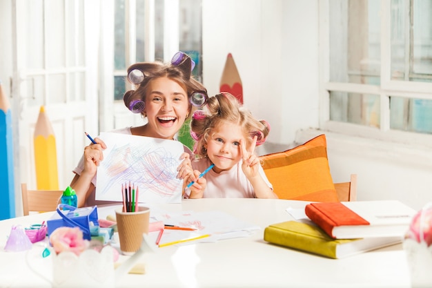 The young mother and her little daughter drawing with pencils at home