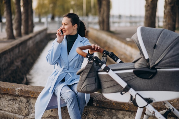 Free photo young mother sitting with baby carriage in park