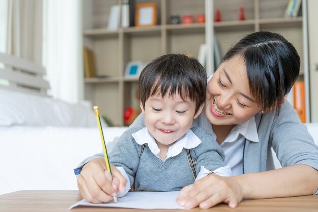 Young mother teaching her son write on paper with love