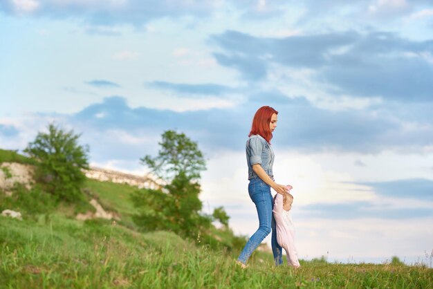 Young mother walking on field holding little daughter's hands