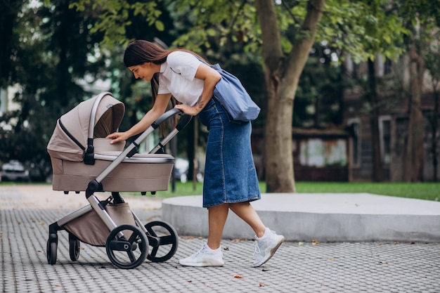 Young mother walking with baby stroller in park