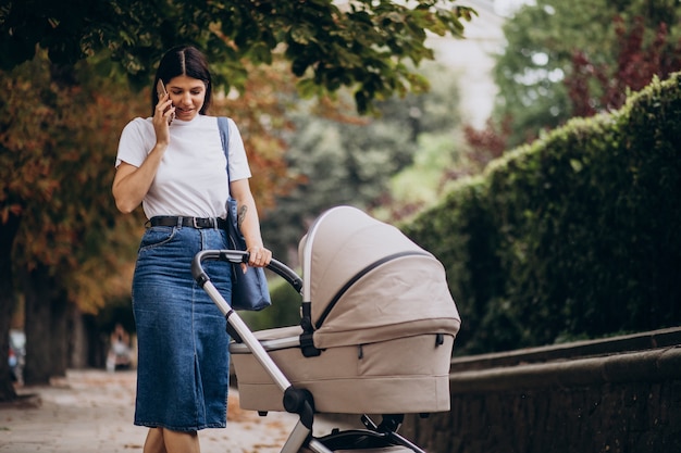 Young mother walking with stroller in park and talking on the phone