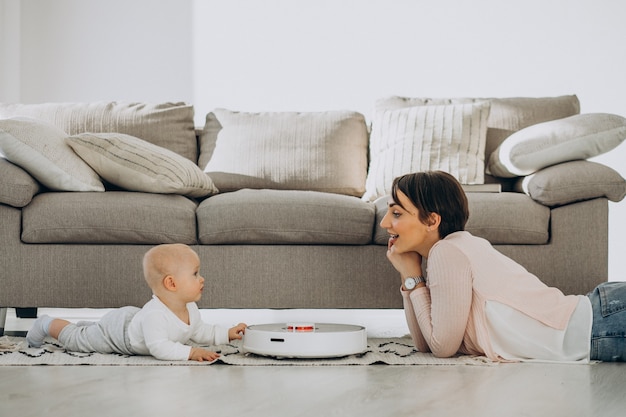 Young mother with toddler son and watching robot vacuum cleaner doing housework