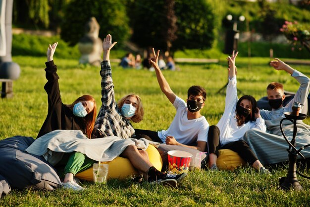 Young multi ethnic group of people watching movie at poof in open air cinema wear at mask during covid coronavirus quarantine