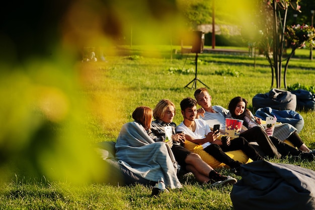 Free photo young multi ethnic group of people watching movie at poof in open air cinema