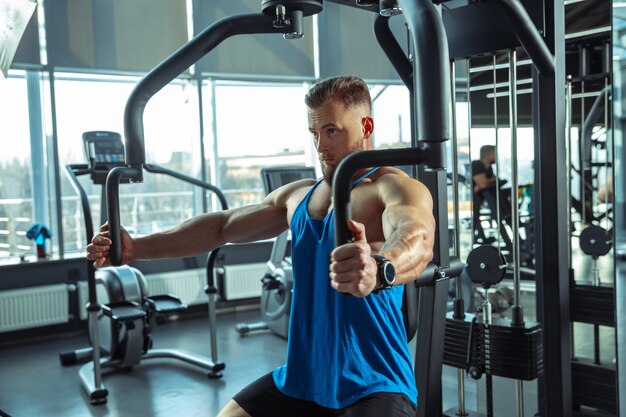 Young muscular athlete training in gym, doing strength exercises, practicing