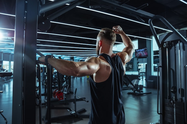 Young muscular caucasian athlete training in gym, doing strength exercises