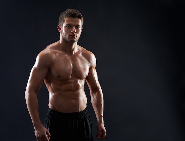 Young muscular fit sportsman posing shirtless on black backgroun