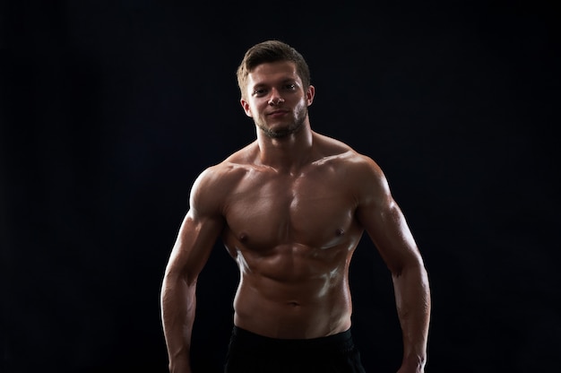 Young muscular fit sportsman posing shirtless on black backgroun