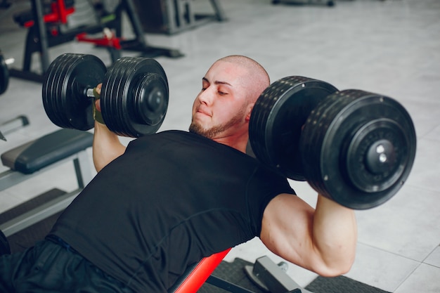 A young and muscular guy in a black t-shirt trains in a gym