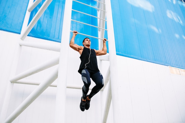 Free photo young muscular man doing pull ups, listening to music in headphones during workout