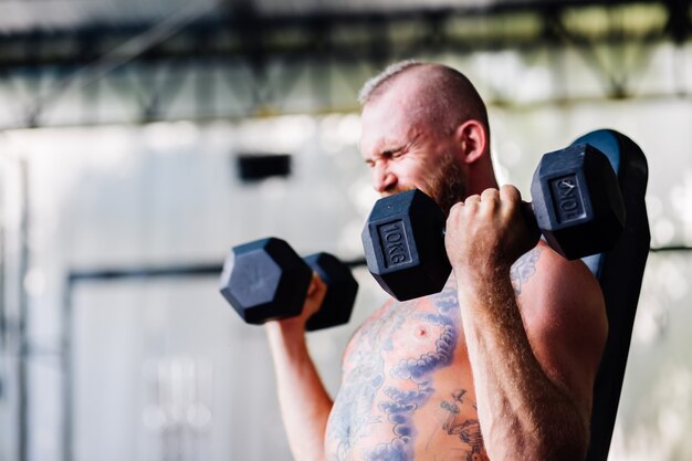 Young muscular tattooed strong muscle bearded european man doing hard exercise