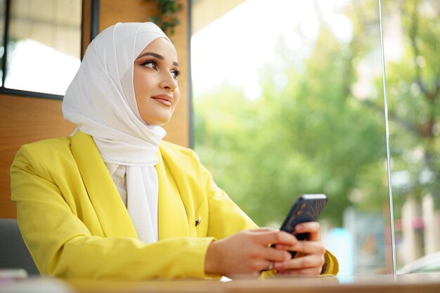 Young muslim woman in hijab using her smartphone in cafe