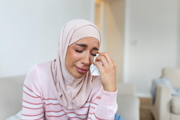 Young Muslim woman sitting in room feeling pain with life problem Crying muslim female holding painful hand suffering from husband violence