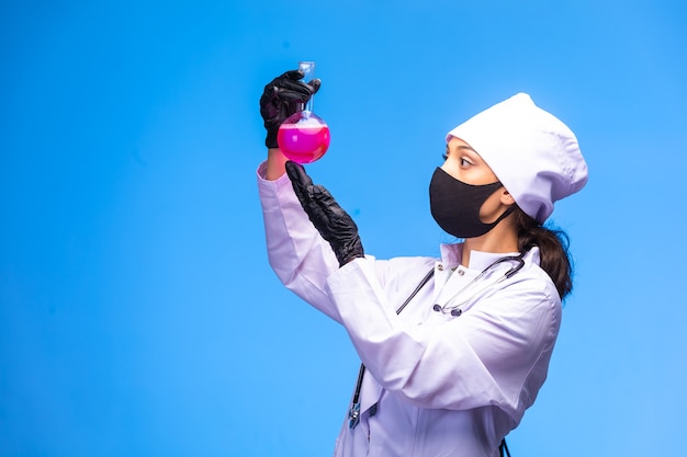 Young nurse in face and hand mask holds a test flask and looks at it. 