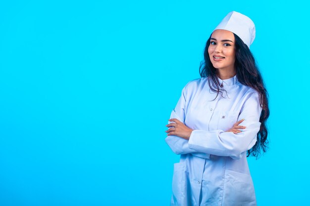 Young nurse in isolated uniform closes arms and smiles. 