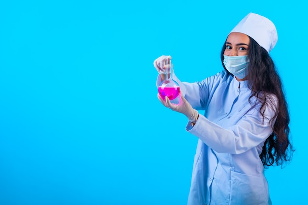 Young nurse in isolated uniform showing chemical flask, profile view.