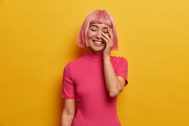 Free Photo young overjoyed woman laughs happily, makes face palm, closes eues from laughter, shows white teeth, has pink hair