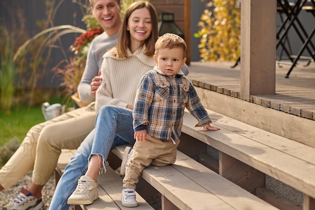 Free photo young parents looking at little son sitting on porch