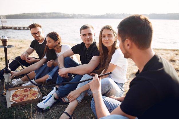 Free photo young people eating pizza and smoking shisha at the beach