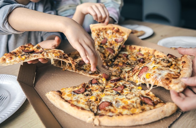 Free photo young people taking slices of hot pizza from cardboard box at table