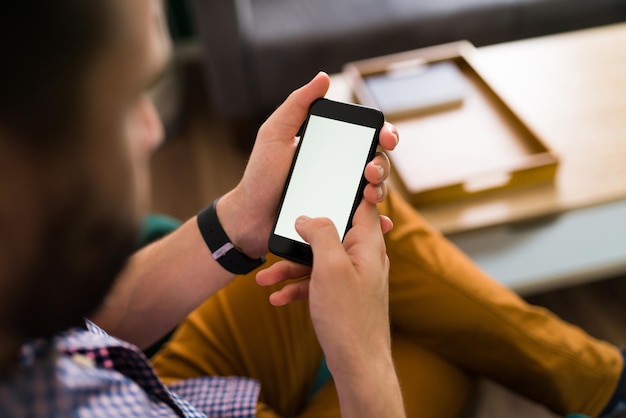 Young person using his smartphone while sitting at home and looking at a blank screen with copyspace